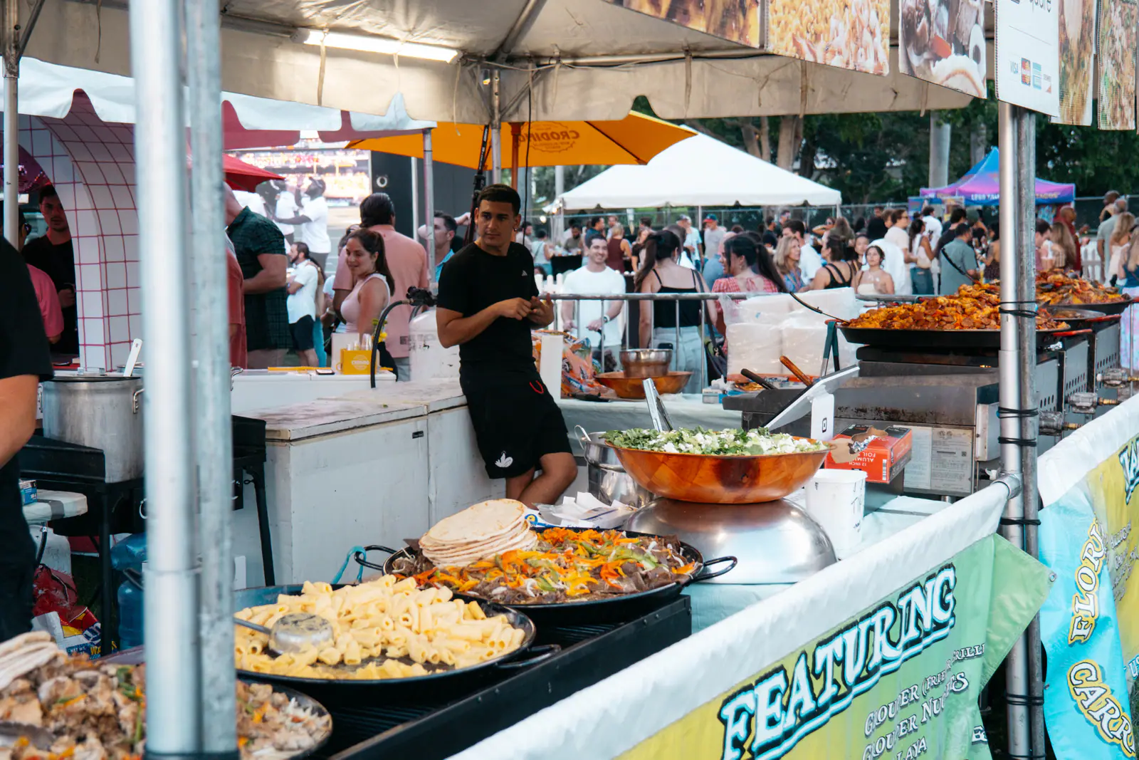 Paella pans and global bites at a food tent, with the festival crowd behind