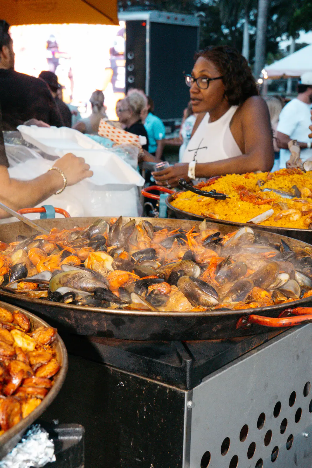 A vendor serving seafood paella from large pans