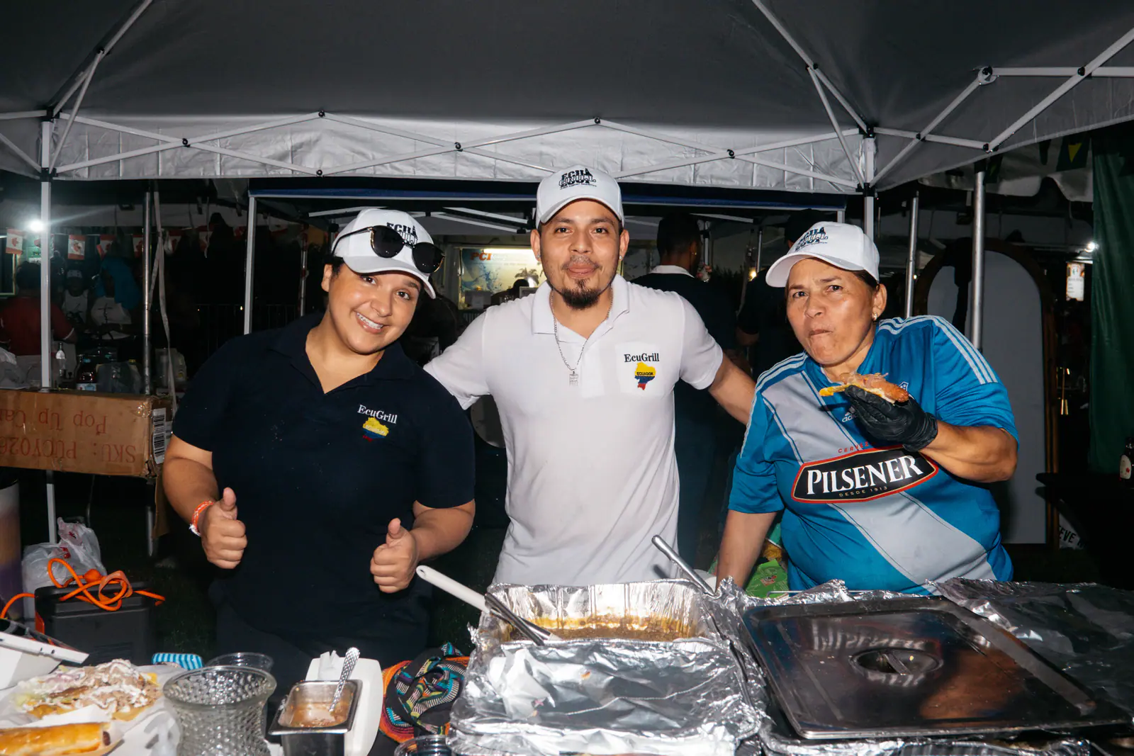 Three food vendors giving a thumbs up behind their serving trays